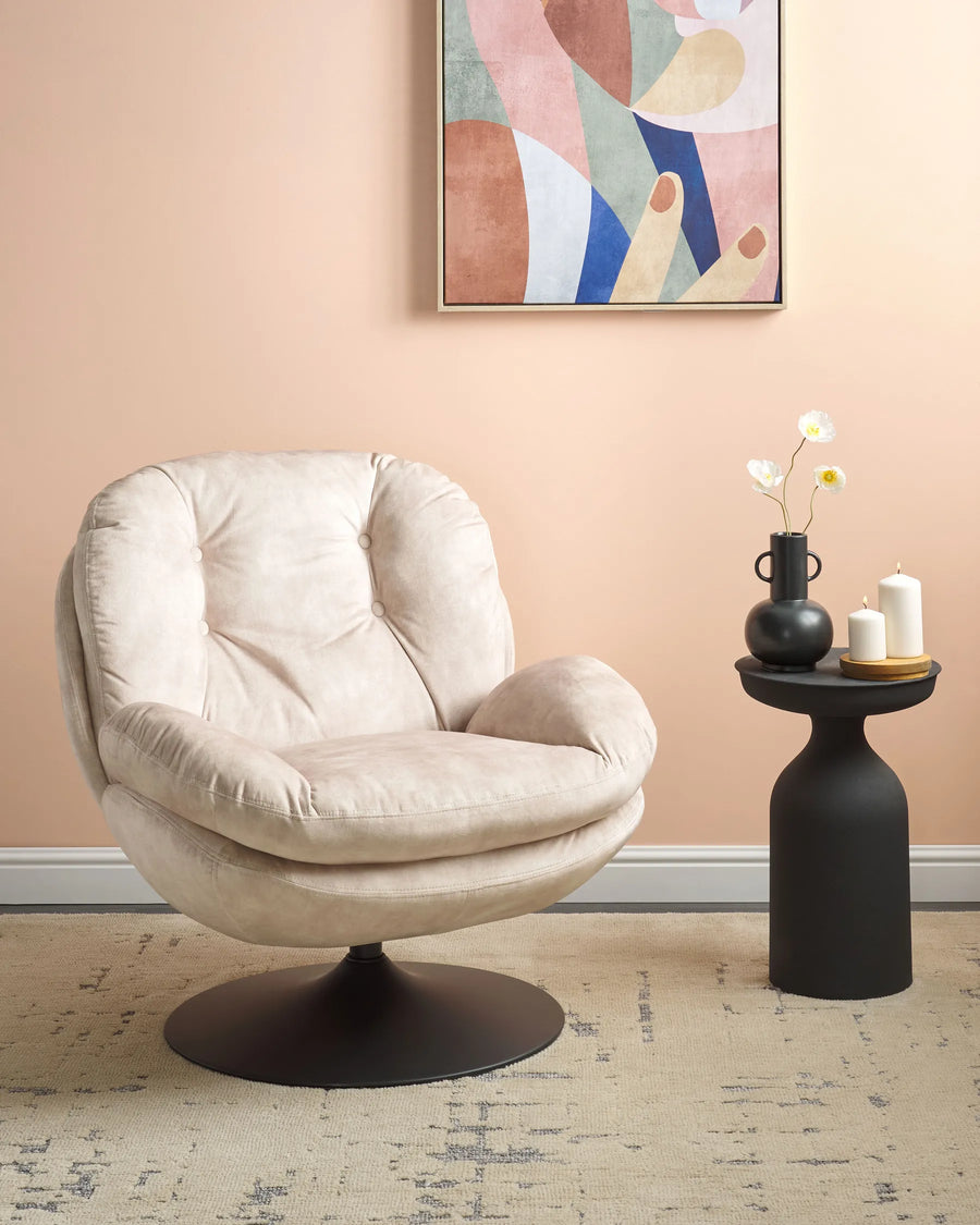 Beige armchair in a room with a abstract painting on the wall and a small black table with decor items.