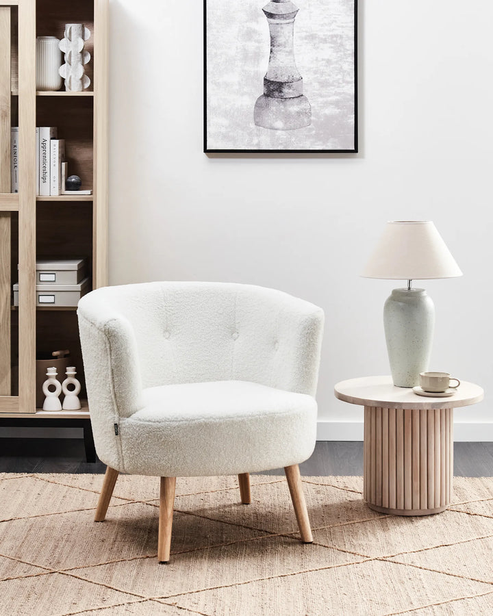 White armchair in a living room setting with a side table and lamp.