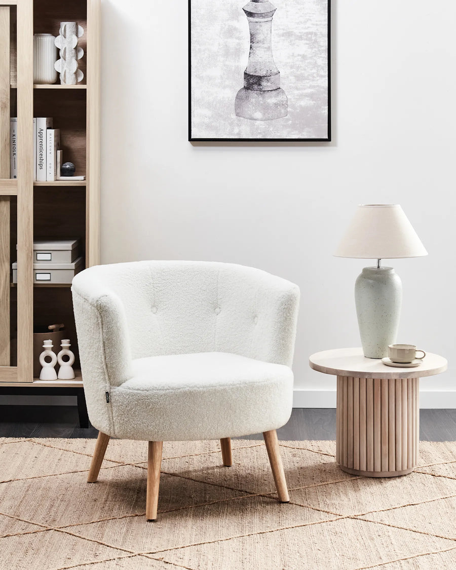 White armchair in a living room setting with a side table and lamp.