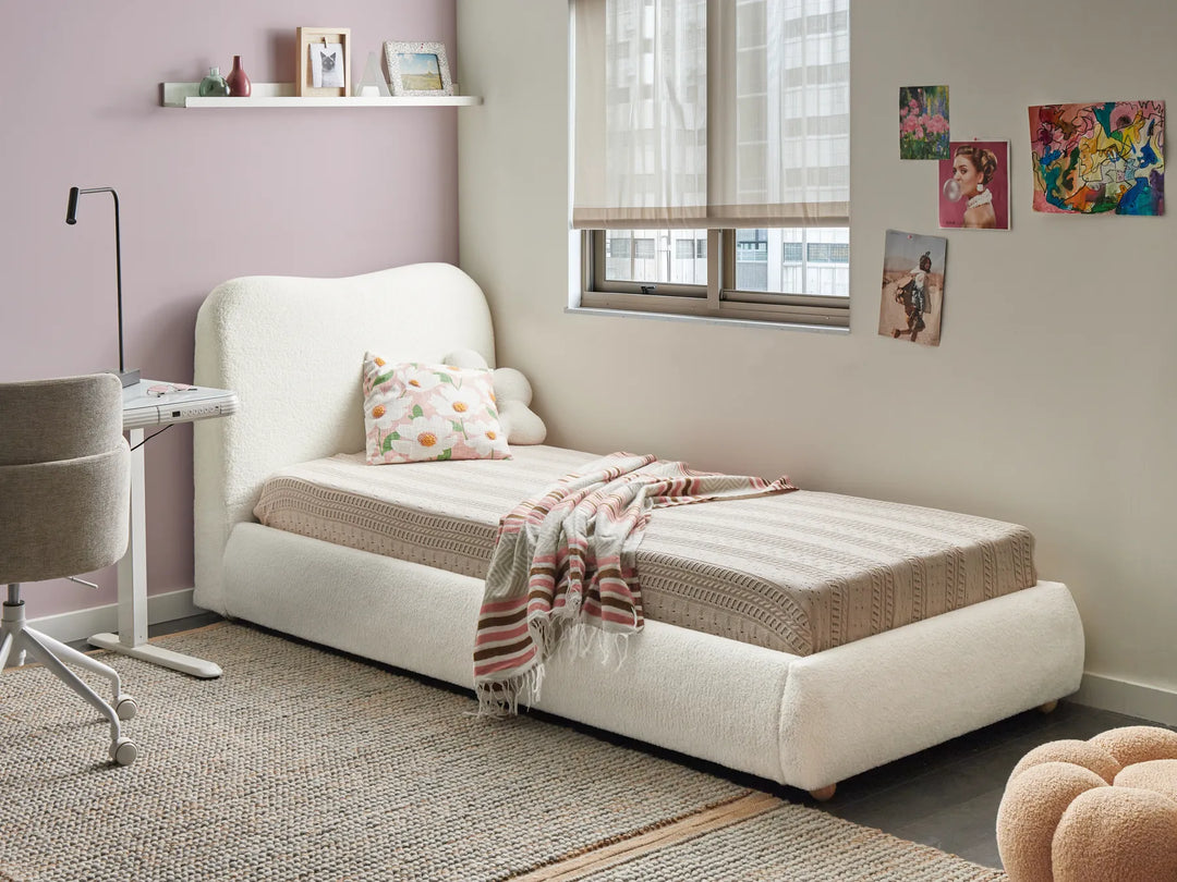 White upholstered bed in a room with a window, shelves, and decorative items.