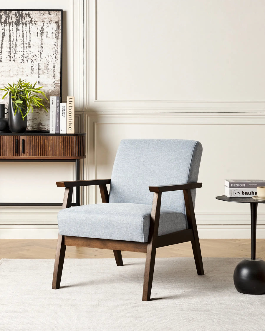 Gray armchair with wooden frame in a room setting with books and a plant.