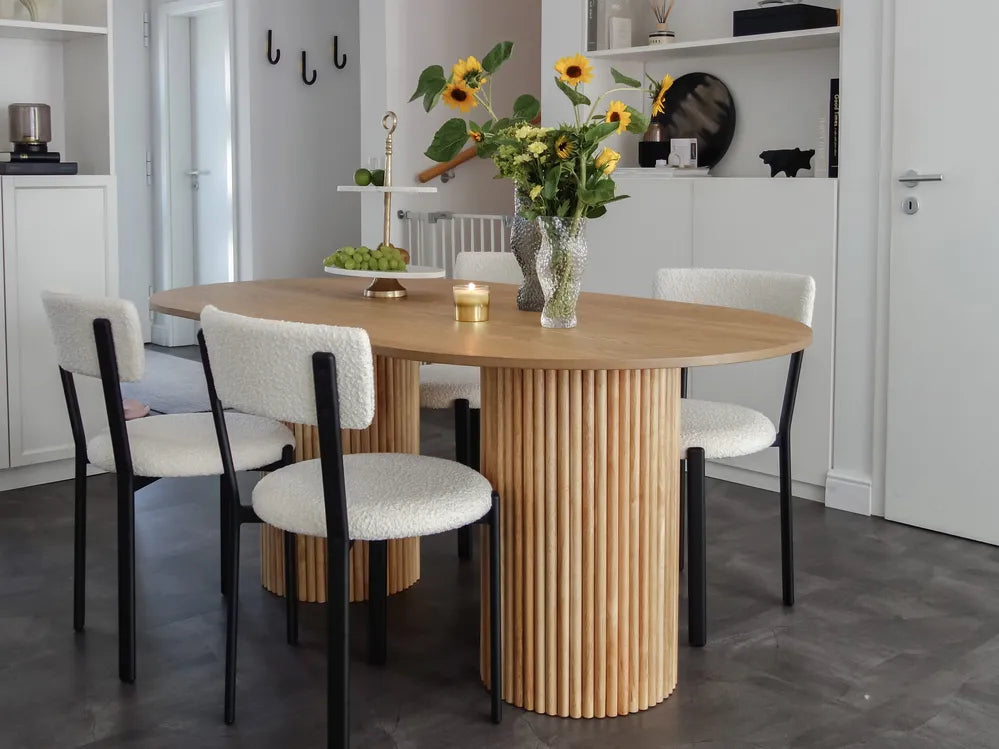 Dining room with a round wooden table and chairs, featuring a vase of flowers.