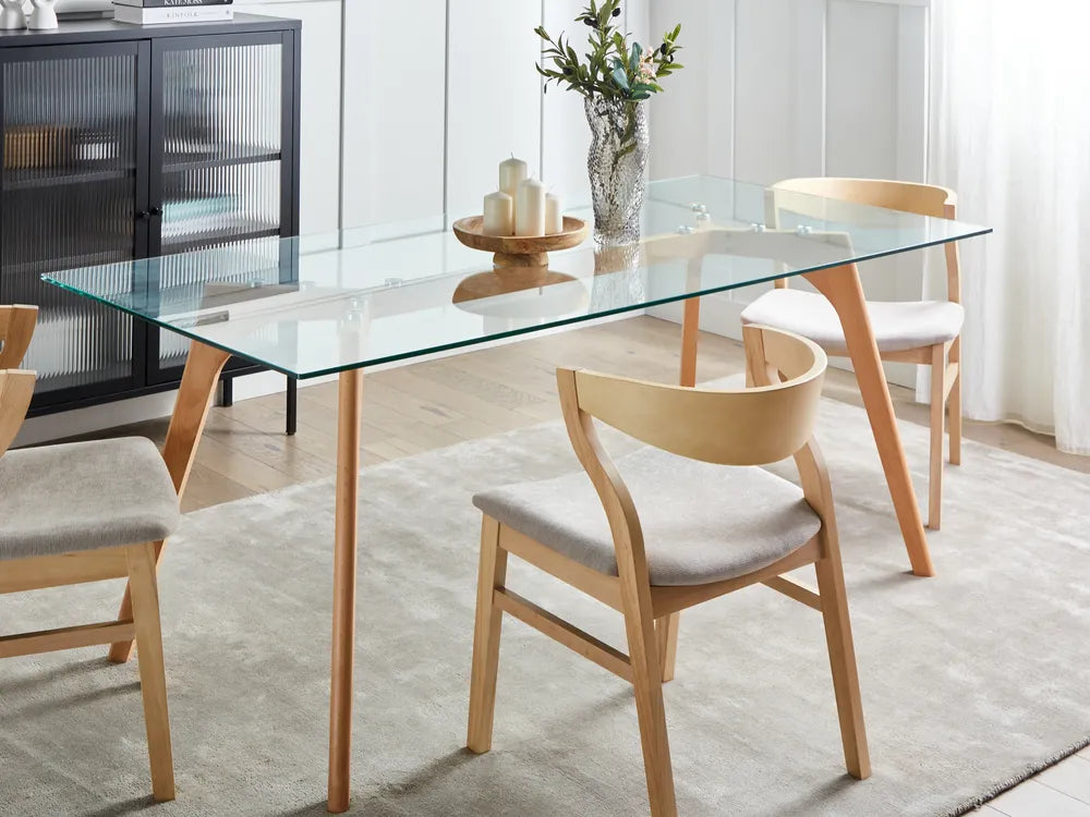 Dining room with glass table and wooden chairs on a light rug.