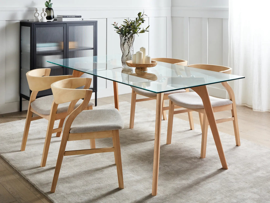 Dining room with a glass table and wooden chairs on a light rug.