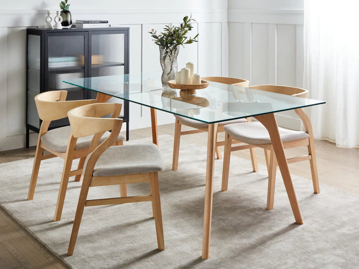 Dining room with a glass table and wooden chairs on a light rug.