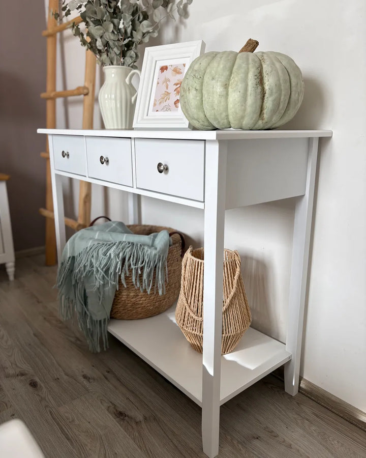 White console table with decorative items including a pumpkin, baskets, and a plant.