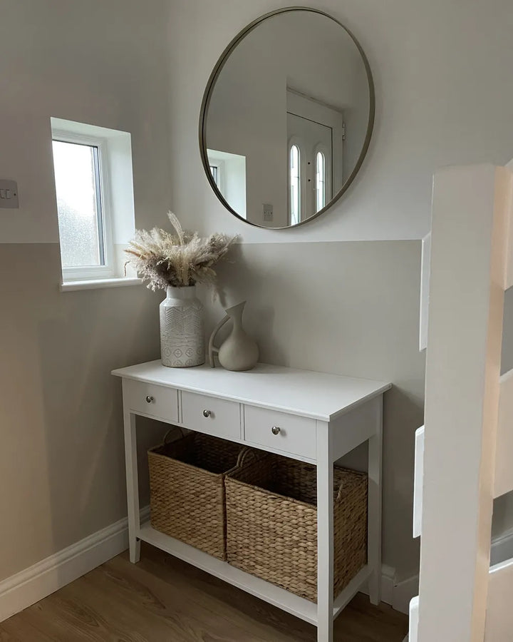 White console table with wicker baskets and decorative vases in a room with a round mirror on the wall.