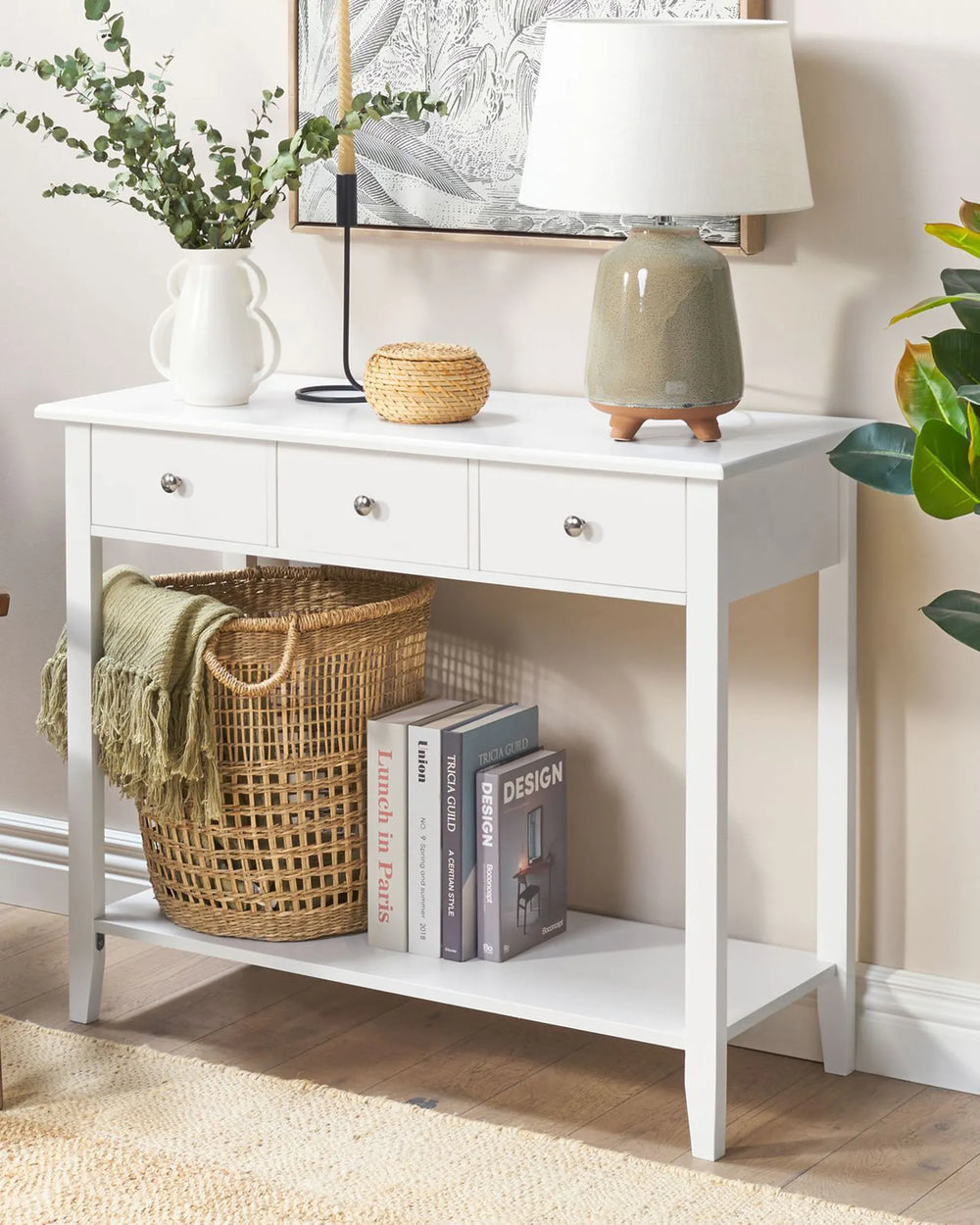 White console table with decorative items including a lamp, books, and a basket in a room setting.