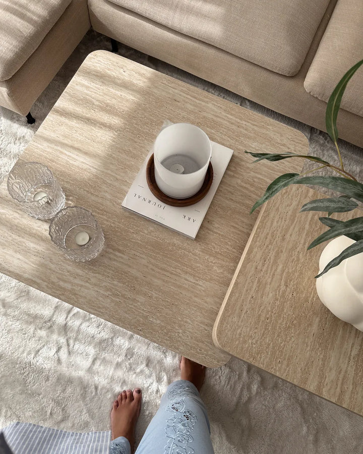 Light wooden coffee table with a white mug, glass, and book on a beige sofa and rug.