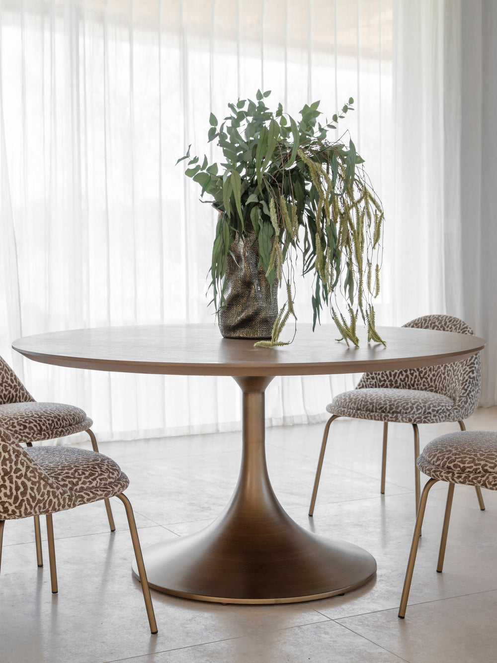 Dining table with chairs and a vase of greenery in a bright room.