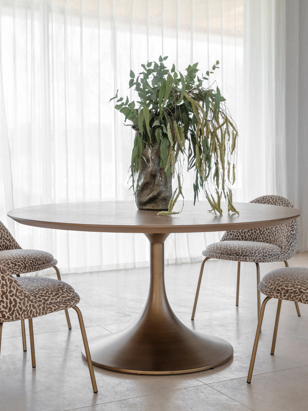 Dining table with chairs and a vase of greenery in a bright room.