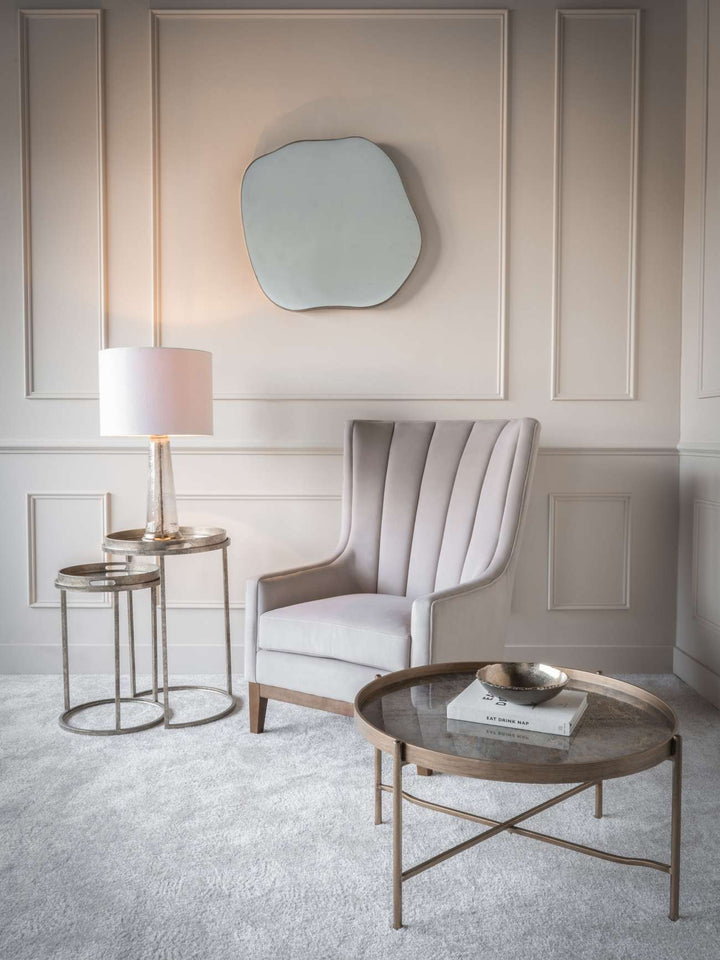 Modern living room with a gray armchair, round coffee table, and wall mirror.