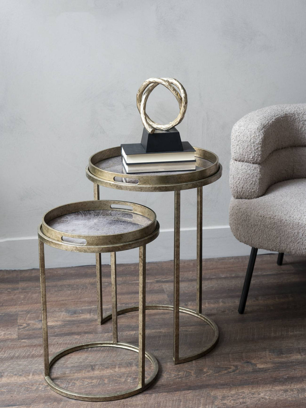 Gold nesting tables with a decorative object on a wooden floor against a gray wall.