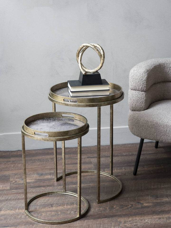 Gold nesting tables with a decorative object on a wooden floor against a gray wall.