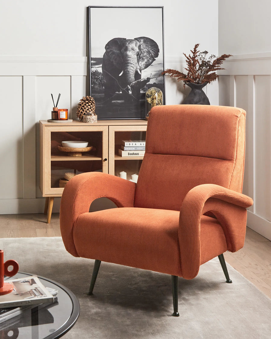 Orange armchair in a living room with a cabinet and decorative items.