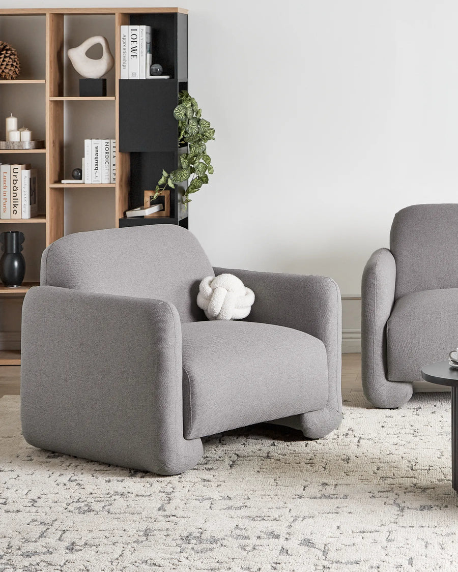 Gray armchair in a modern living room with bookshelf and decor items.