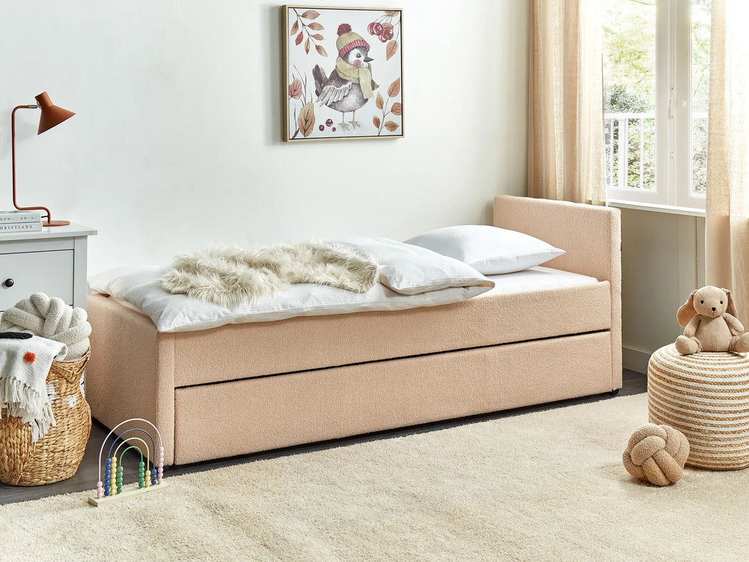 Beige upholstered bed with storage drawers in a child-friendly room with toys and a lamp.