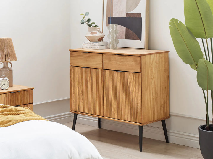 Wooden sideboard in a bedroom with a bed, lamp, and plant.