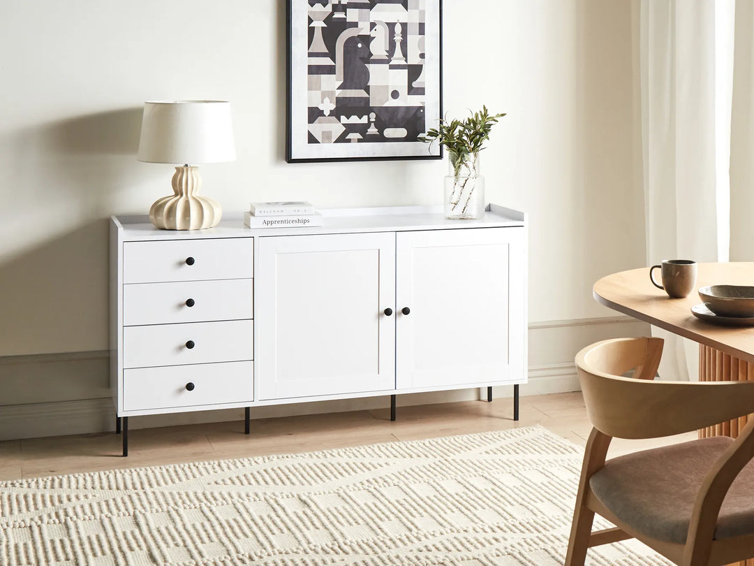 White dresser with drawers and doors in a room with a lamp, plant, and small table.