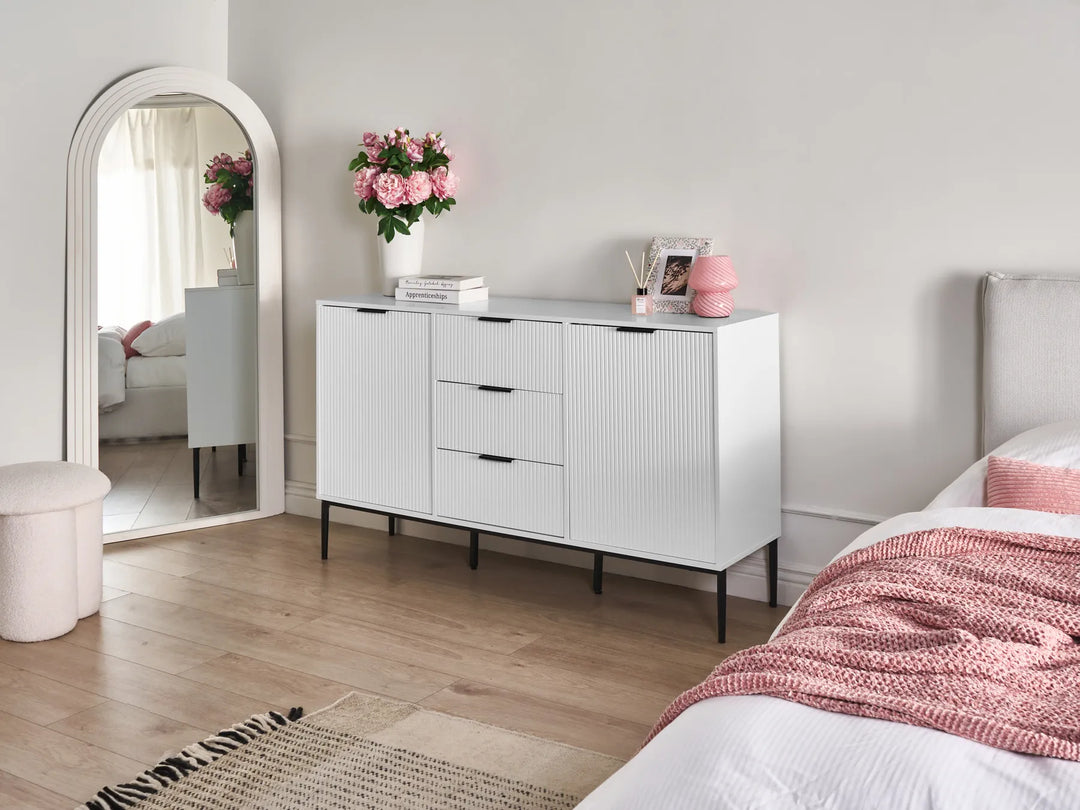 Modern bedroom with a white dresser, bed with pink blanket, and decorative items.