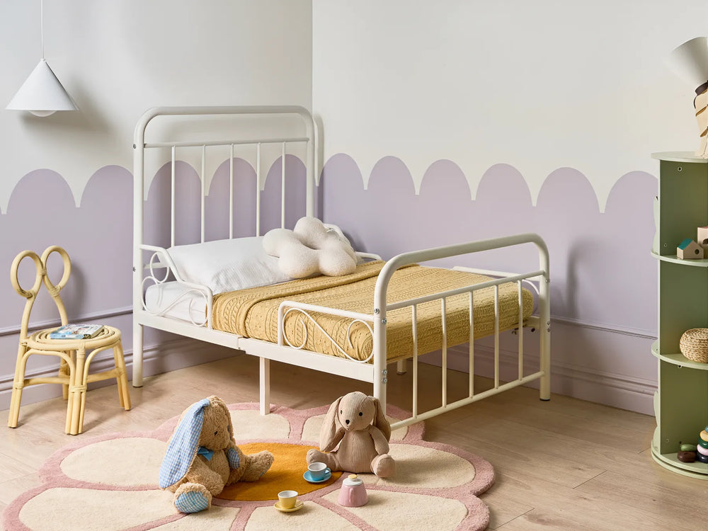 Children's bedroom with a white metal bed, toys, and a colorful rug.