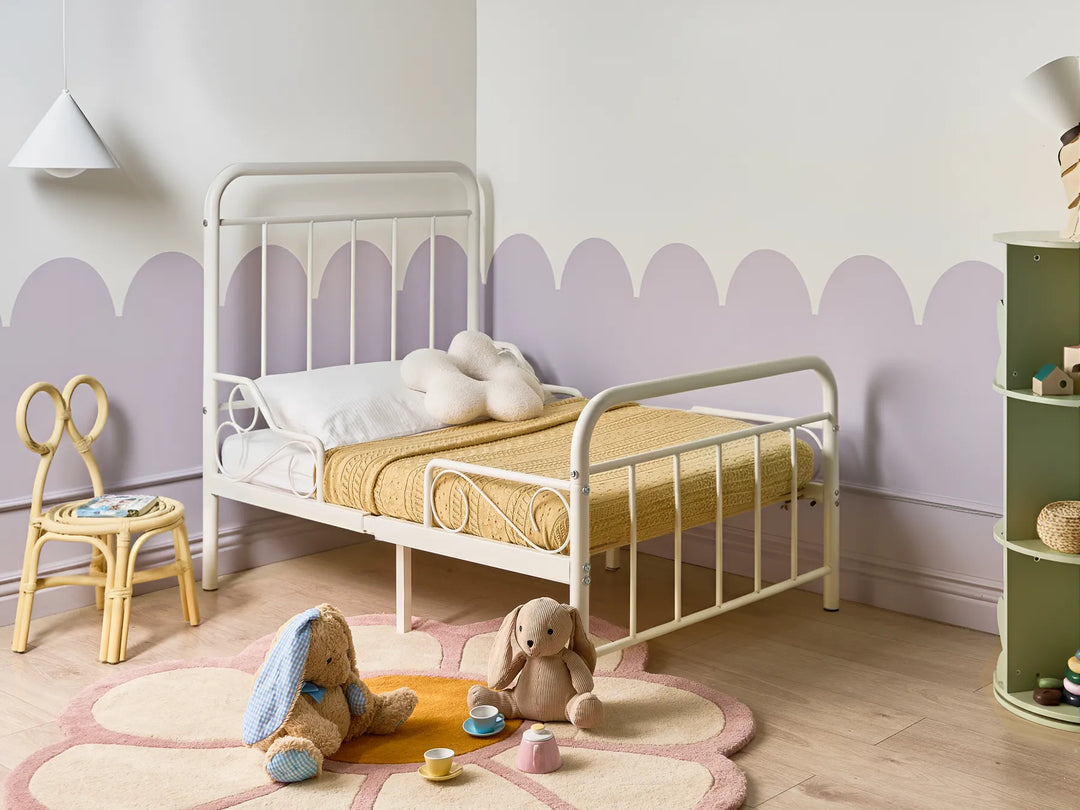 Children's bedroom with a white metal bed, toys, and a colorful rug.