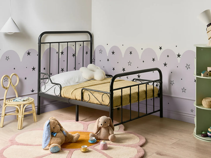 Children's bedroom with a black metal bed, teddy bears, and decorative elements.