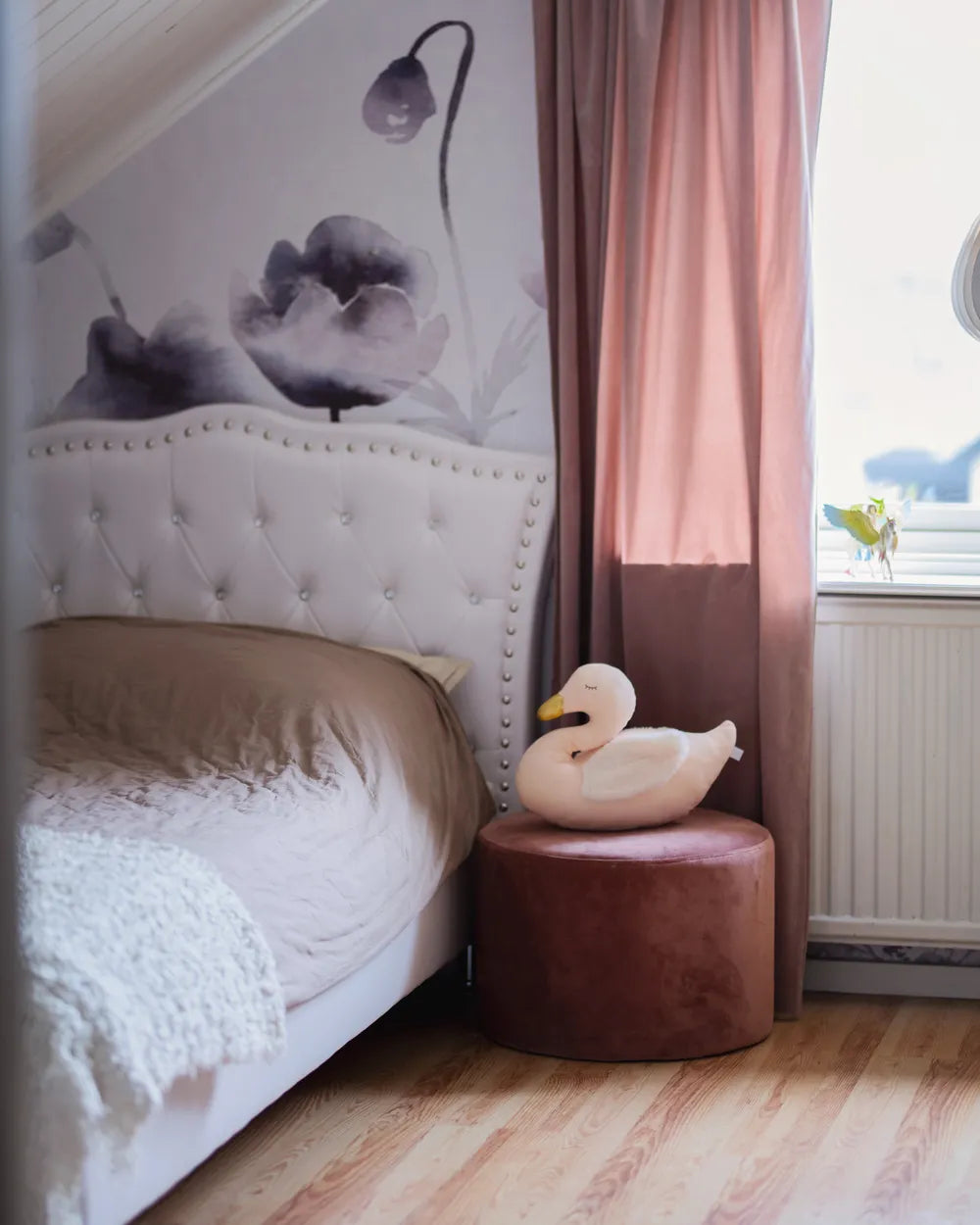 Bedroom with tufted headboard, pink ottoman, and swan-shaped pillow.