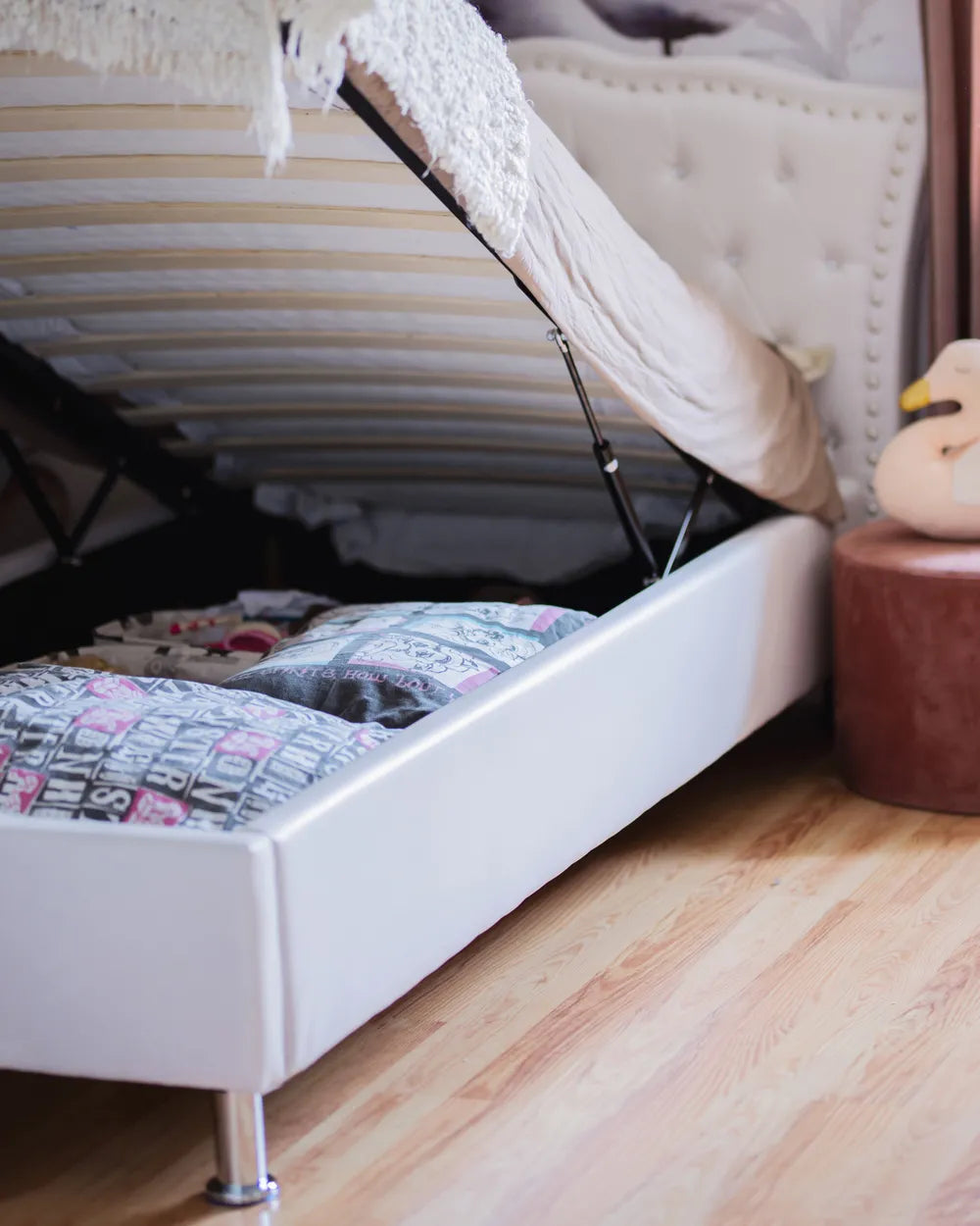 White bed with storage compartment under the mattress, wooden floor.