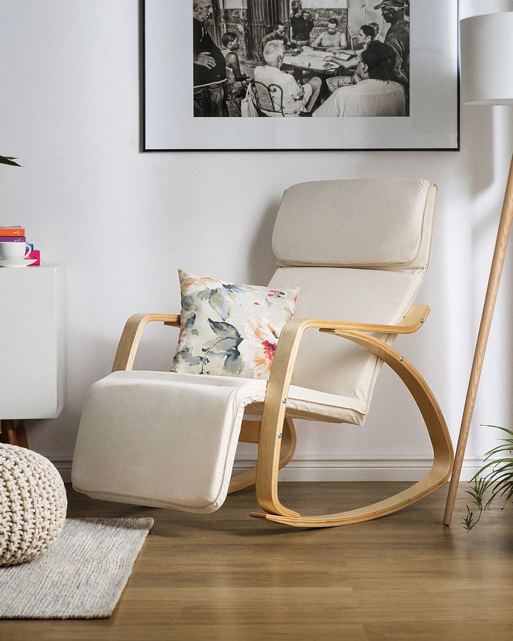Beige rocking chair with a floral pillow in a room with a framed picture on the wall.