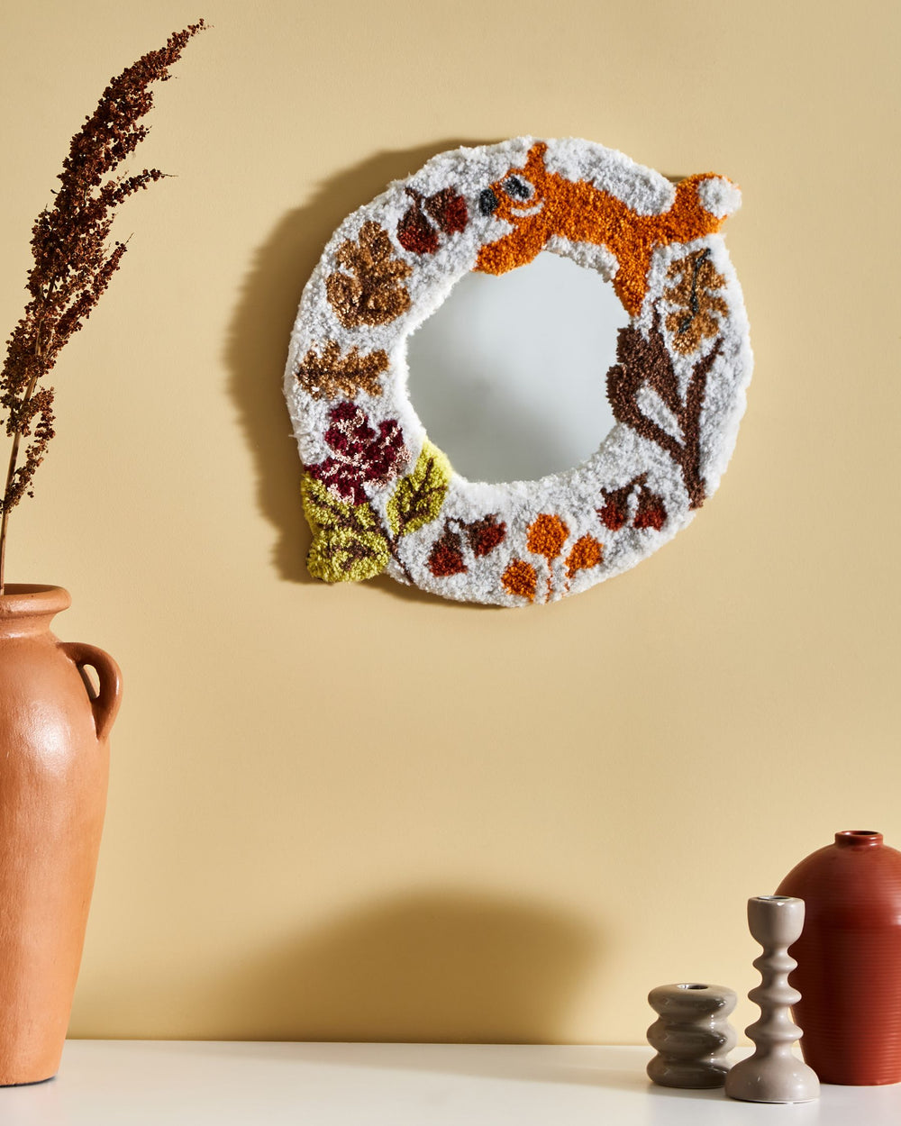 Decorative mirror with floral patterns on a beige wall with vases and candles.