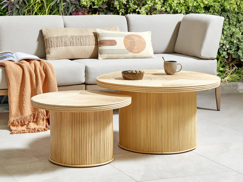 Wicker coffee table with a cup and small bowl on a patio with a sofa and cushions in the background.