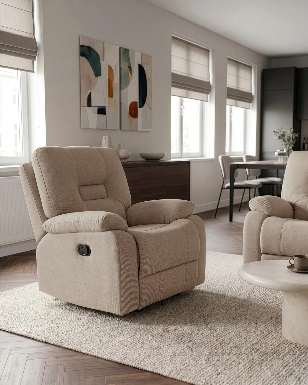 A beige upholstered recliner chair shown in a modern living room setting with a matching armchair, rug, windows, and abstract wall art.