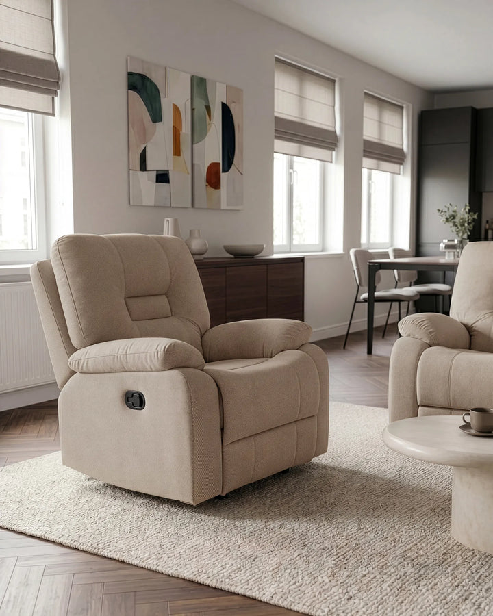 A beige upholstered recliner chair shown in a modern living room setting with a matching armchair, rug, windows, and abstract wall art.