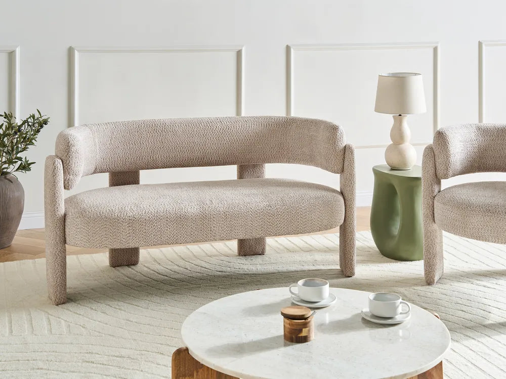 Modern beige armchair and sofa in a living room setting with a coffee table and lamp.