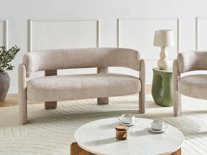 Modern beige armchair and sofa in a living room setting with a coffee table and lamp.