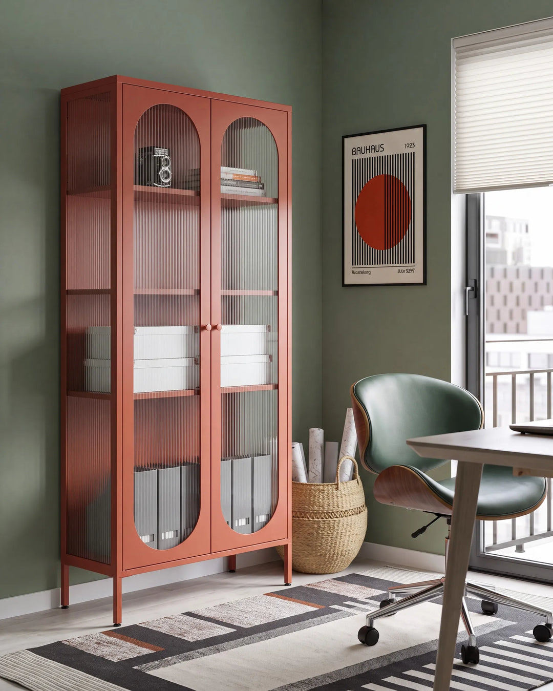 A tall rust-orange metal storage cabinet with two arched glass doors stands in a styled room corner next to a desk and chair.