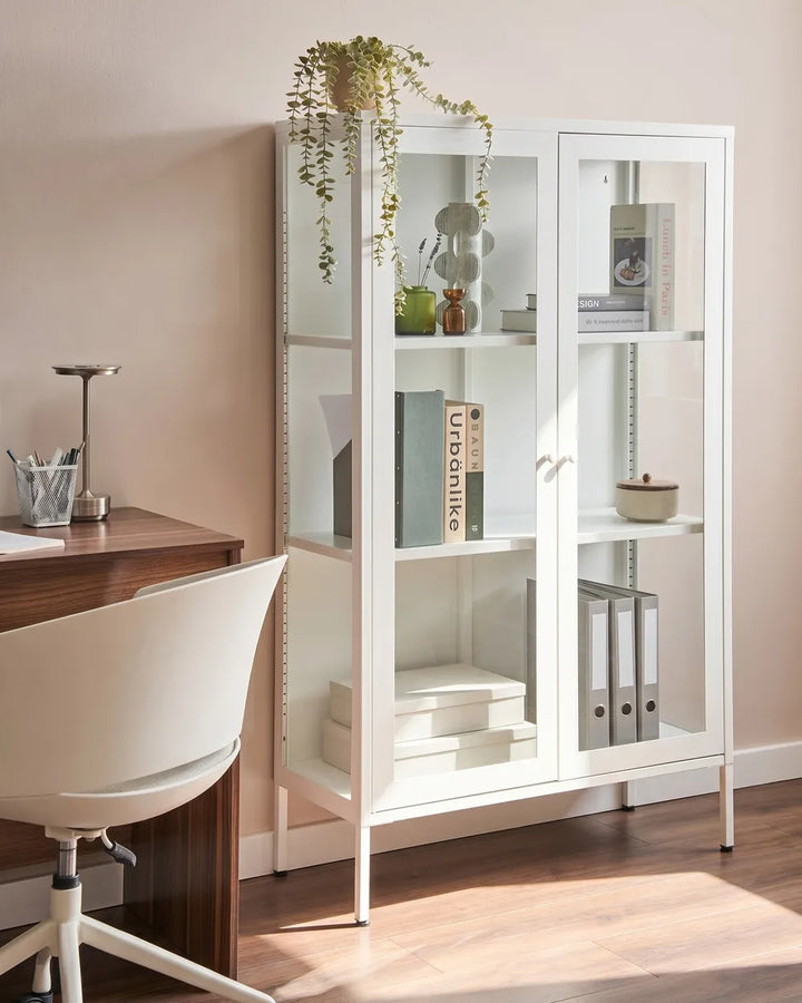 A tall white glass-front bookcase with open shelves and two glass doors, styled in a home office next to a wooden desk and white chair.