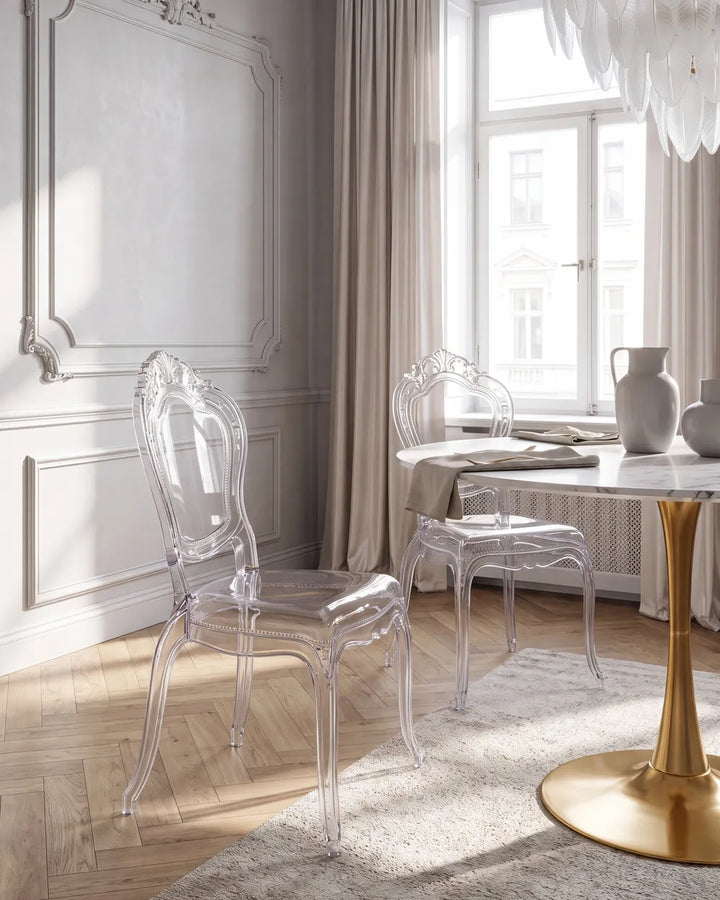 Two transparent acrylic dining chairs in a bright, elegant room with light wood floors, beige walls, and a window.