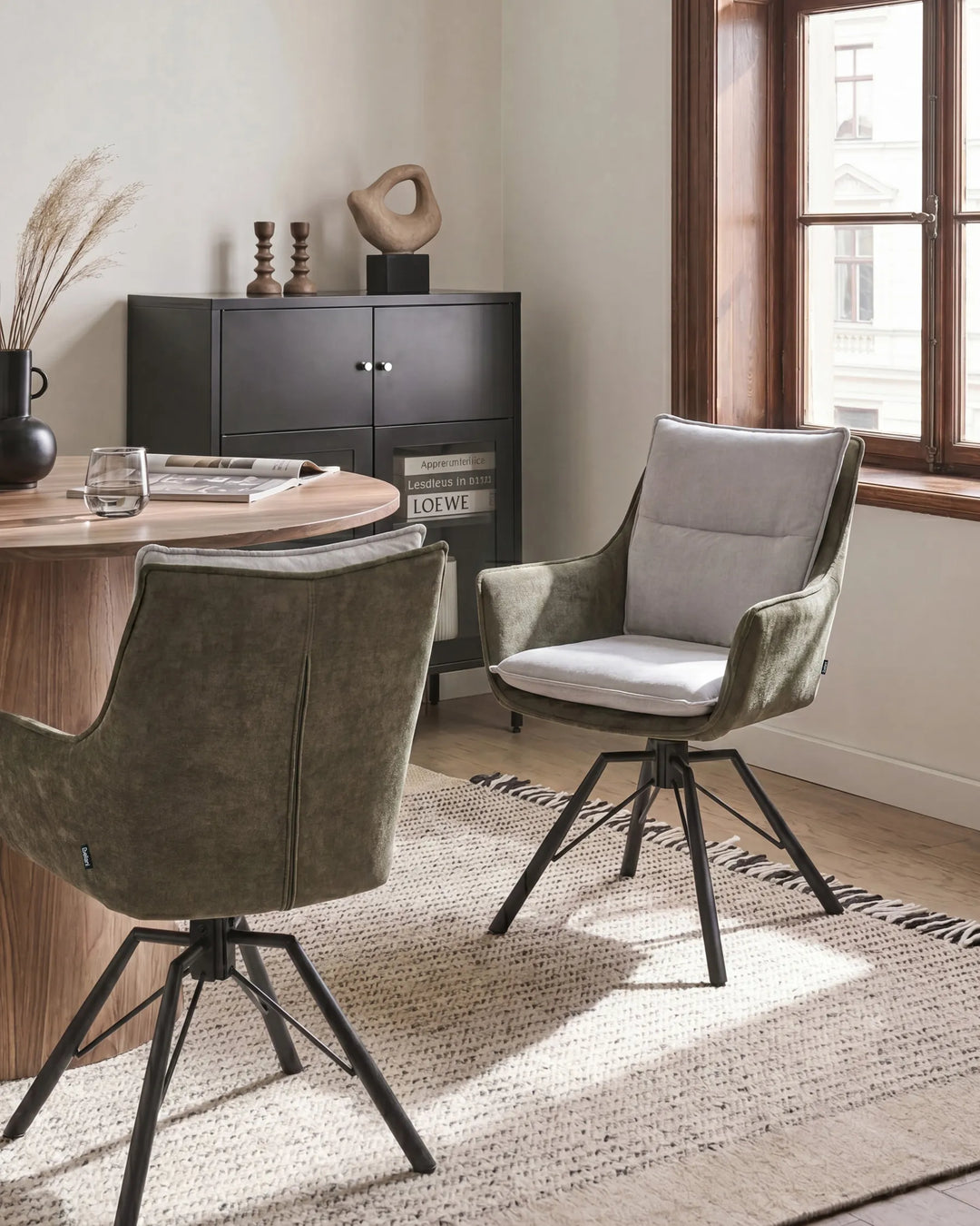 Two modern swivel dining chairs in a styled dining room setting. One chair is upholstered in textured olive green velvet with a white seat cushion, and the other is shown from the back in olive green velvet.