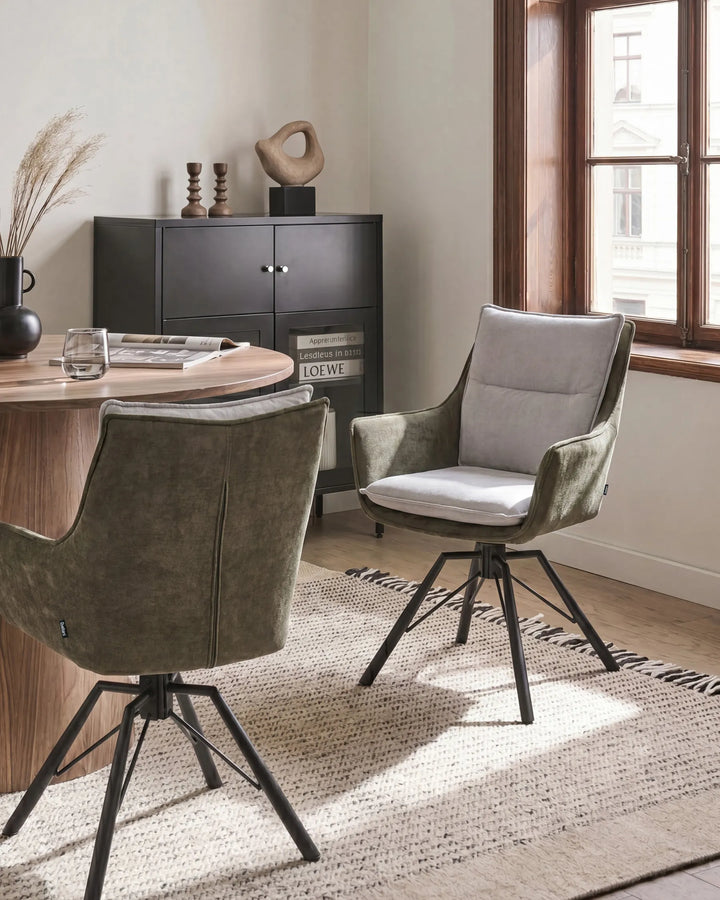Two modern swivel dining chairs in a styled dining room setting. One chair is upholstered in textured olive green velvet with a white seat cushion, and the other is shown from the back in olive green velvet.