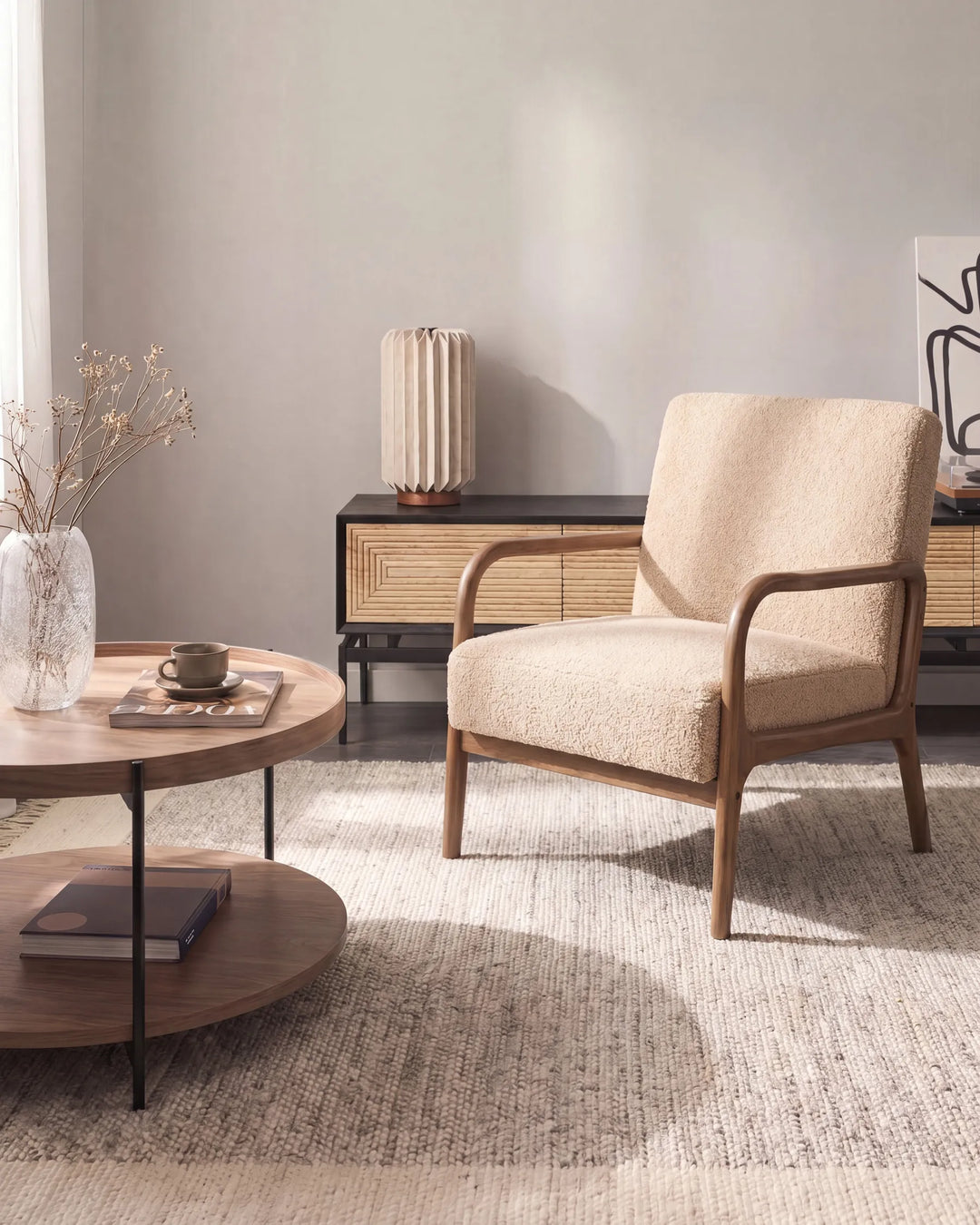 A mid-century modern accent chair with textured beige upholstery and a natural wood frame, positioned in a styled living room next to a round wooden coffee table.