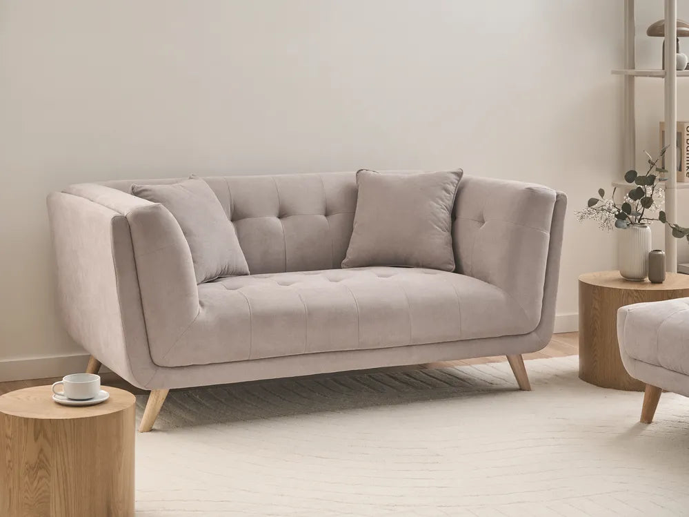 A light beige tufted loveseat sofa with tapered wooden legs, styled in a minimalist living room setting with wooden side tables and neutral decor.