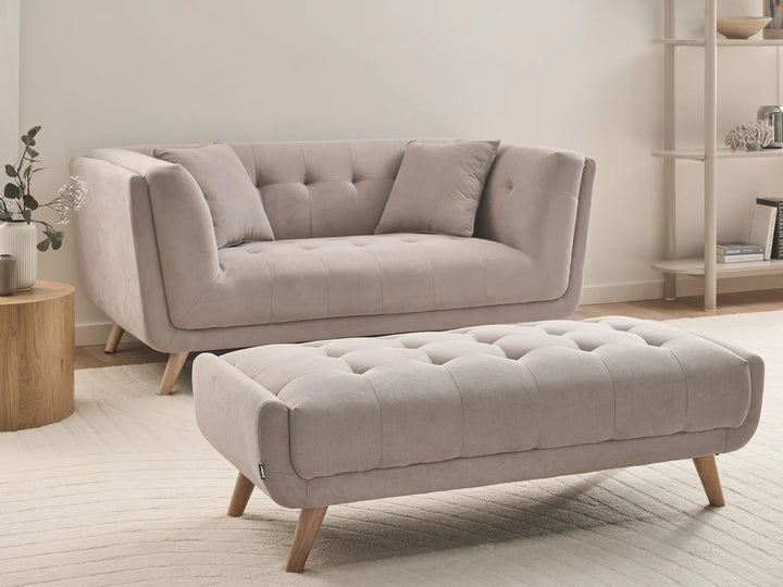 Beige sofa and ottoman in a living room setting with a neutral color palette.