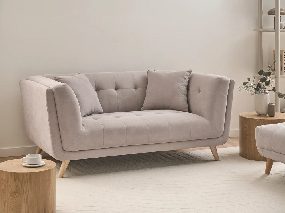 A light beige tufted loveseat sofa with wooden legs, styled in a minimalist living room setting with wooden side tables and a neutral rug.