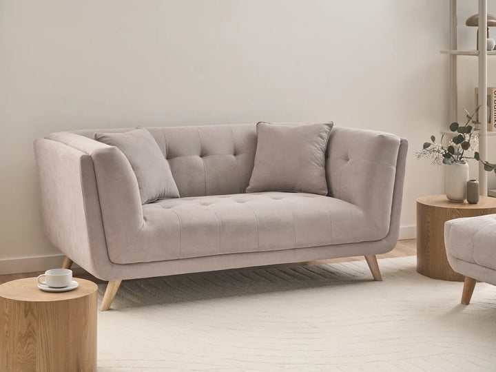 A light beige tufted loveseat sofa with wooden legs, styled in a minimalist living room setting with wooden side tables and a neutral rug.