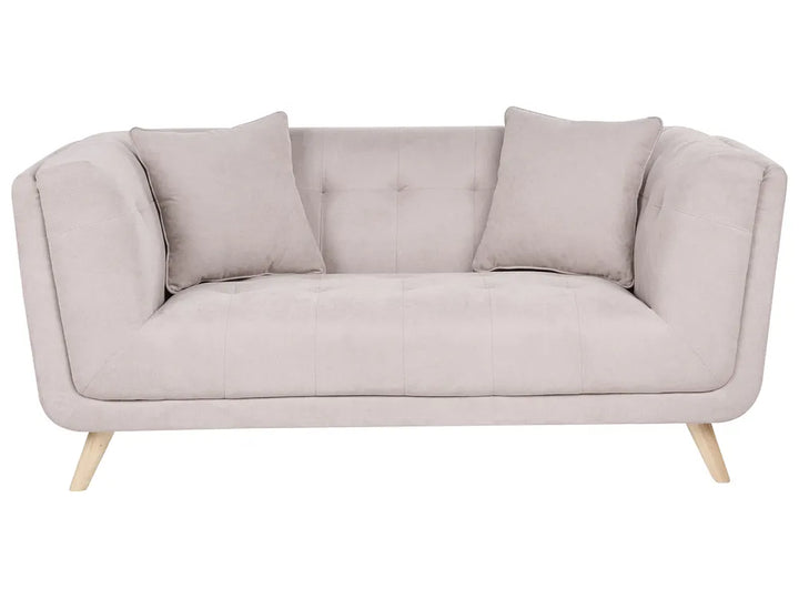 A light beige upholstered loveseat with two matching throw pillows and light wood legs, shown against a plain white background.