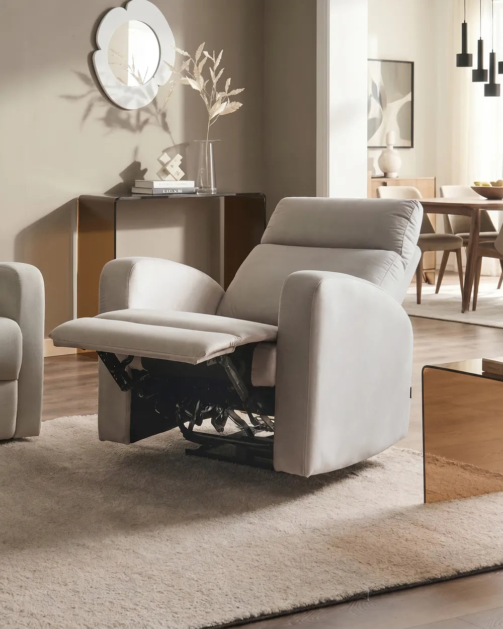 A light beige upholstered recliner chair with the footrest extended, shown in a modern living room setting with a matching rug, sideboard, and warm wood furniture in the background.
