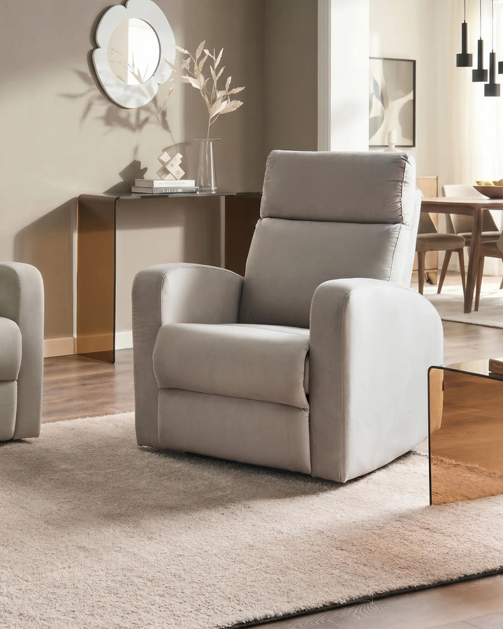 A light beige upholstered recliner chair shown in a modern living room setting with a matching rug, side table, and warm wood flooring.