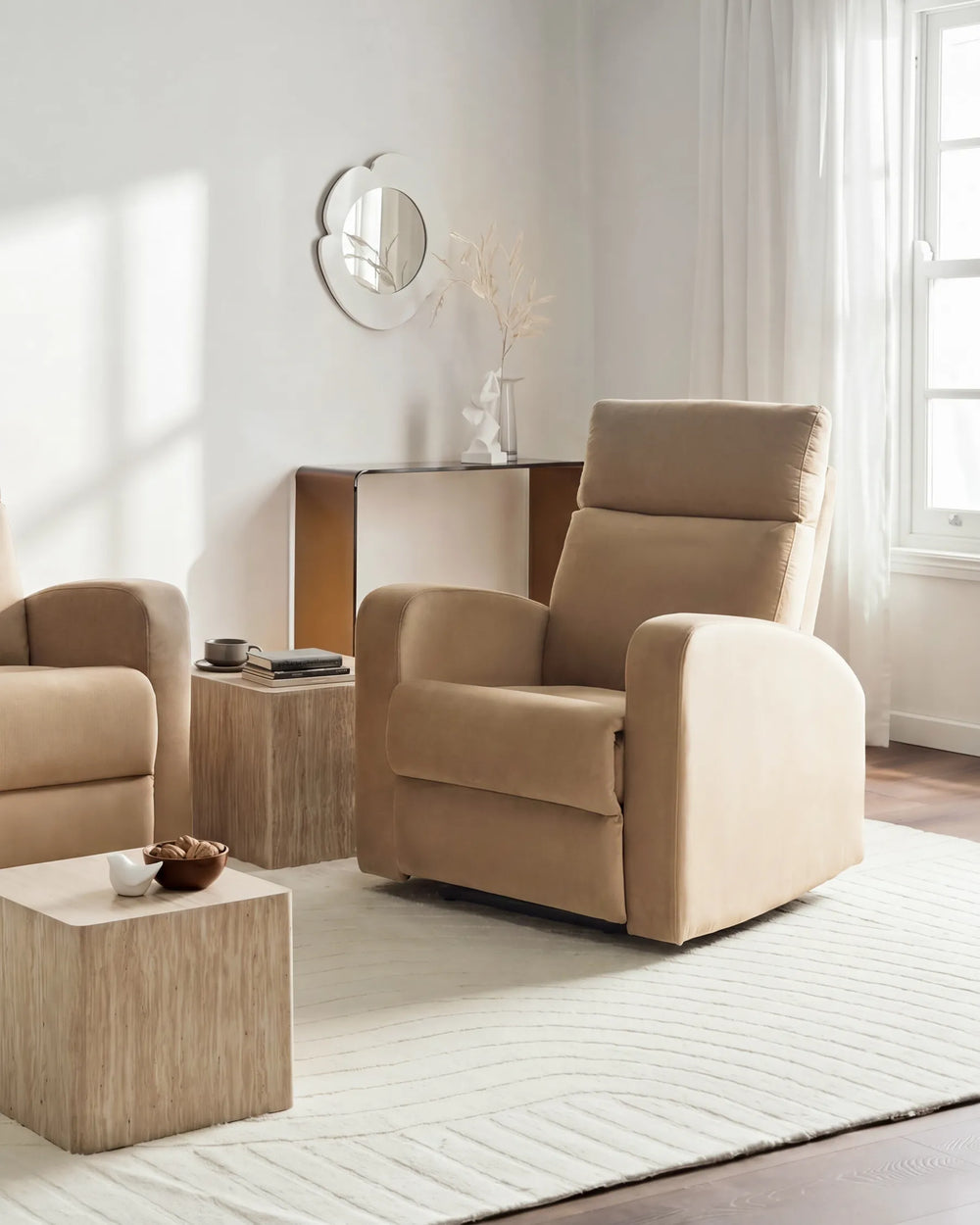 A beige upholstered recliner chair shown in a bright, modern living room with matching furniture, a side table, rug, and window.